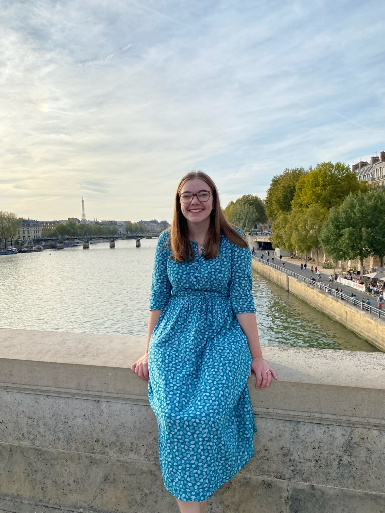 Hannah Fremont-Brown, sitting on a wall overlooking a river.