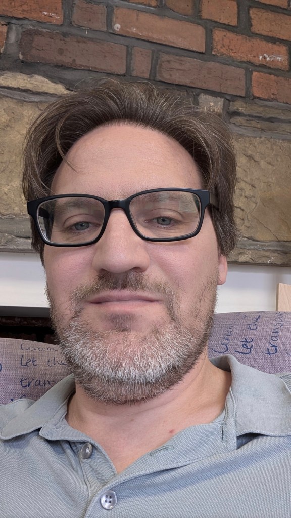 A head and shoulders image of Paul, wearing glasses and an open-necked polo shirt.